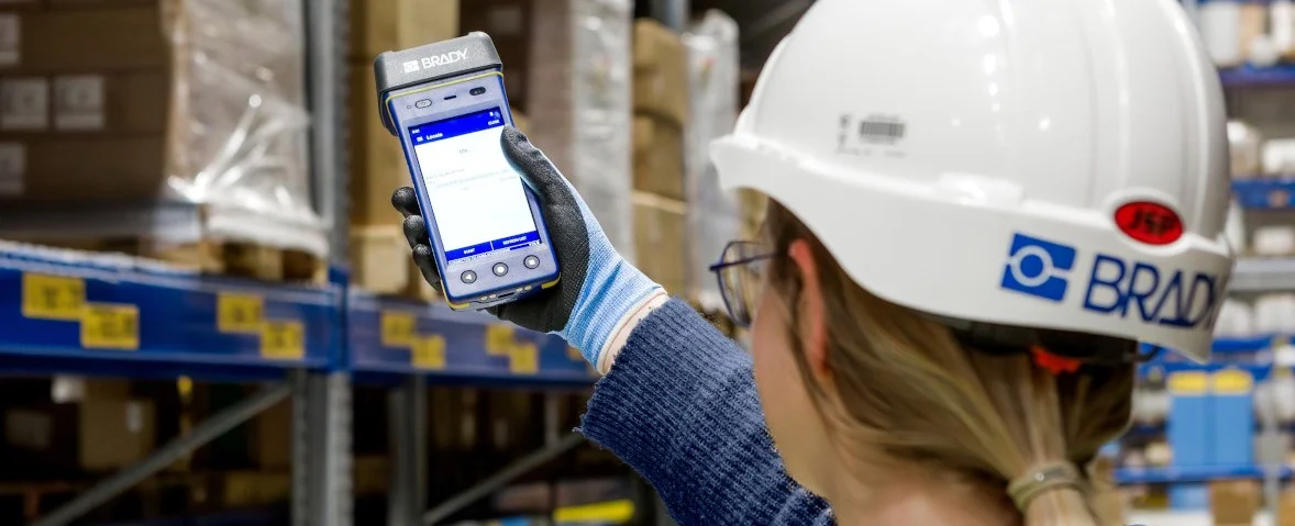 Worker wearing a Brady hard hat scanning a package with a handheld mobile scanner